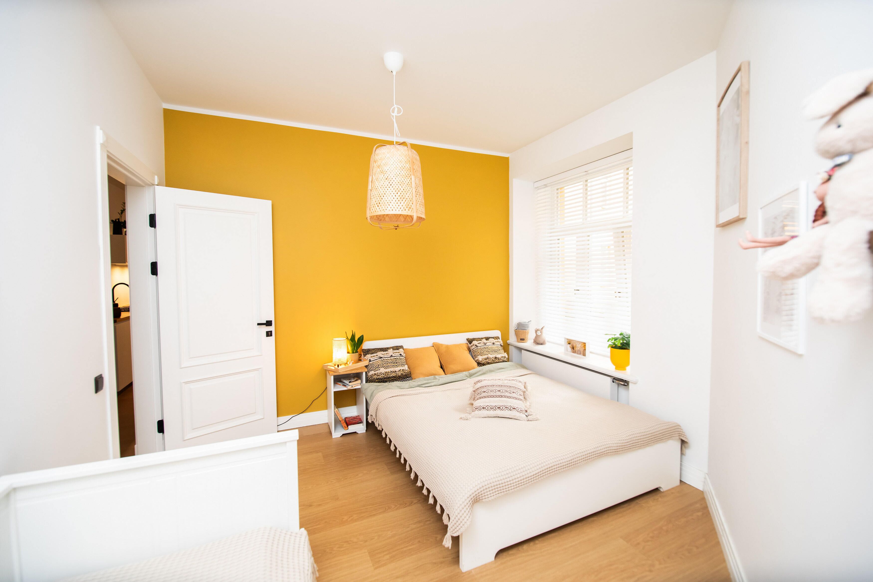 Une chambre à coucher avec un lit, une table de chevet, une lampe et une fenêtre avec des stores.