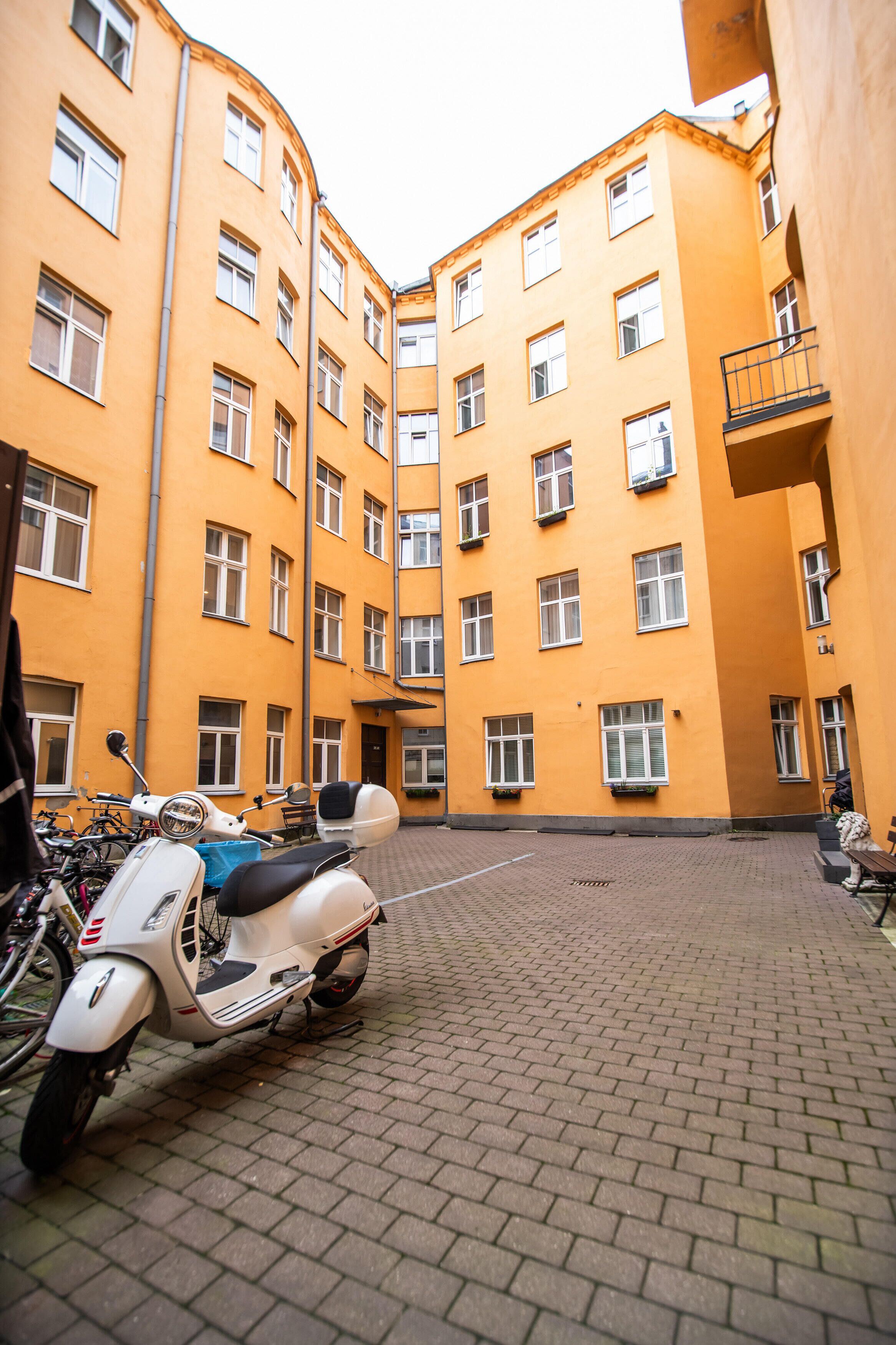 Une cour intérieure où est garé un scooter blanc, au centre, entourée d’immeubles jaunes dotés de nombreuses fenêtres et de balcons.