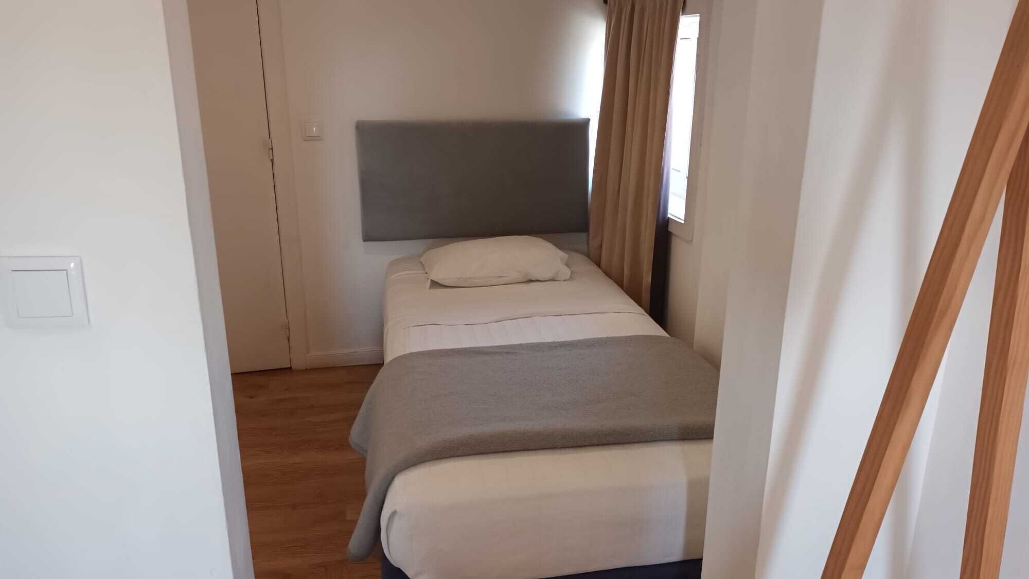 Habitación pequeña con cama individual, cabecera, mesita de noche y ventana con cortinas.