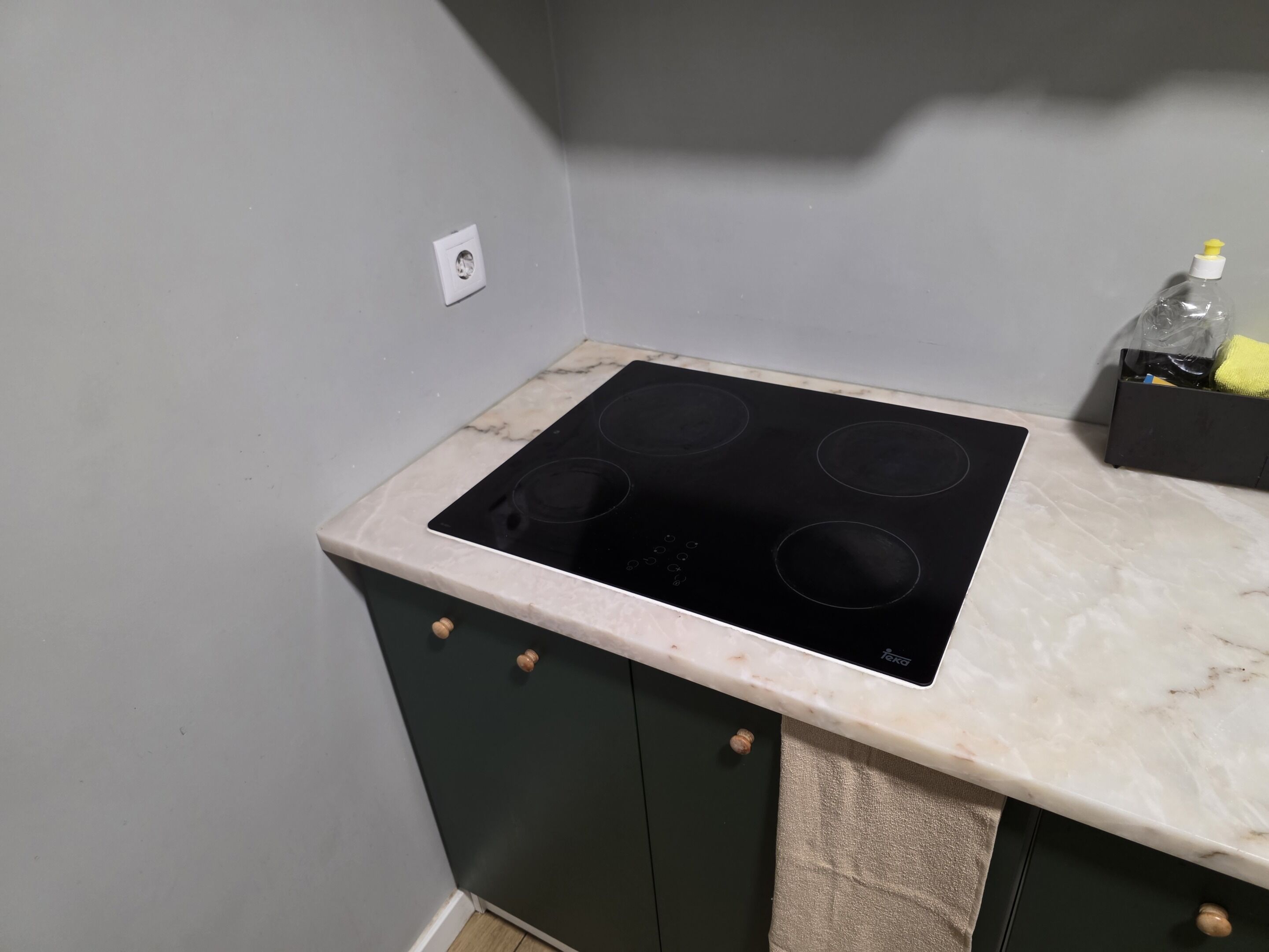 A kitchen with a black induction cooktop, a marble countertop, and dark green cabinets.