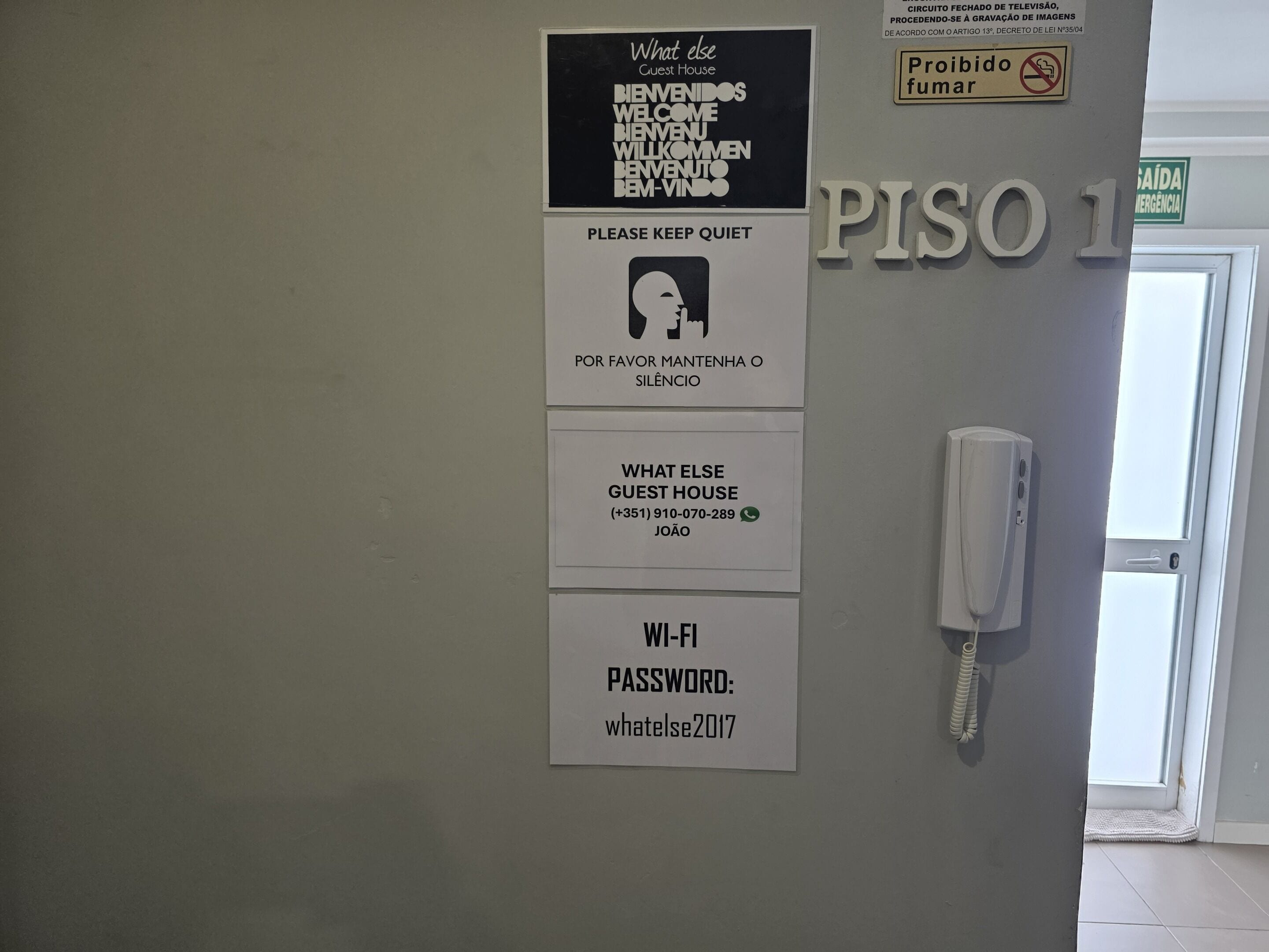 Una pared con varios letreros, incluyendo el letrero de 'What Else Guest House', un letrero que dice 'Silencio, por favor', un letrero con la contraseña de 'Wi-Fi' y un letrero que indica 'Prohibido fumar'.