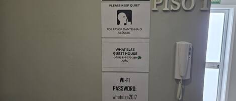 Una pared con varios letreros, incluyendo el letrero de 'What Else Guest House', un letrero que dice 'Silencio, por favor', un letrero con la contraseña de 'Wi-Fi' y un letrero que indica 'Prohibido fumar'.