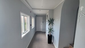En gang med grå vægge, flisegulv, en potteplante og en trappe med trætrin.