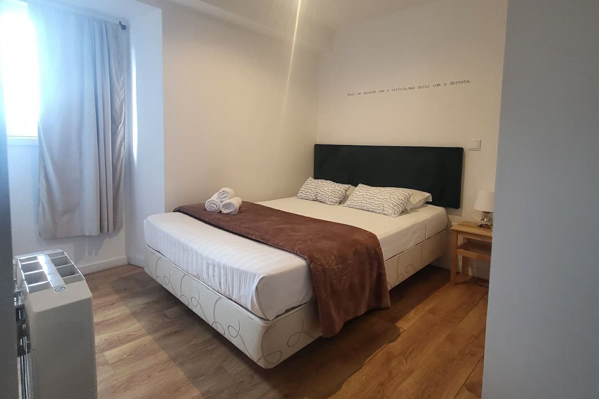 A bedroom with a bed, a bedside table, a lamp, and a window with curtains.
