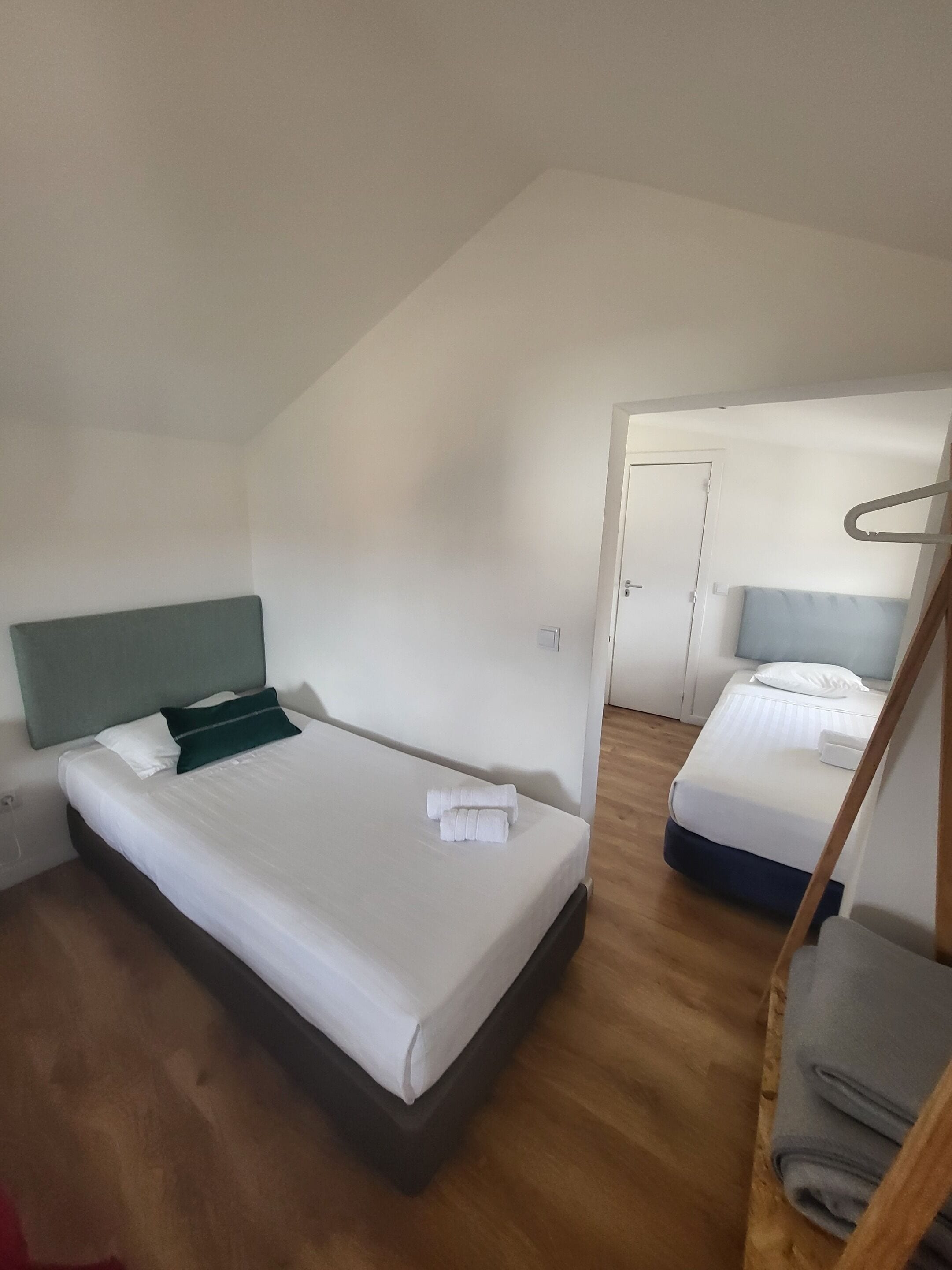 A modern, well-lit room with a large bed, a smaller bed, and a wooden floor.