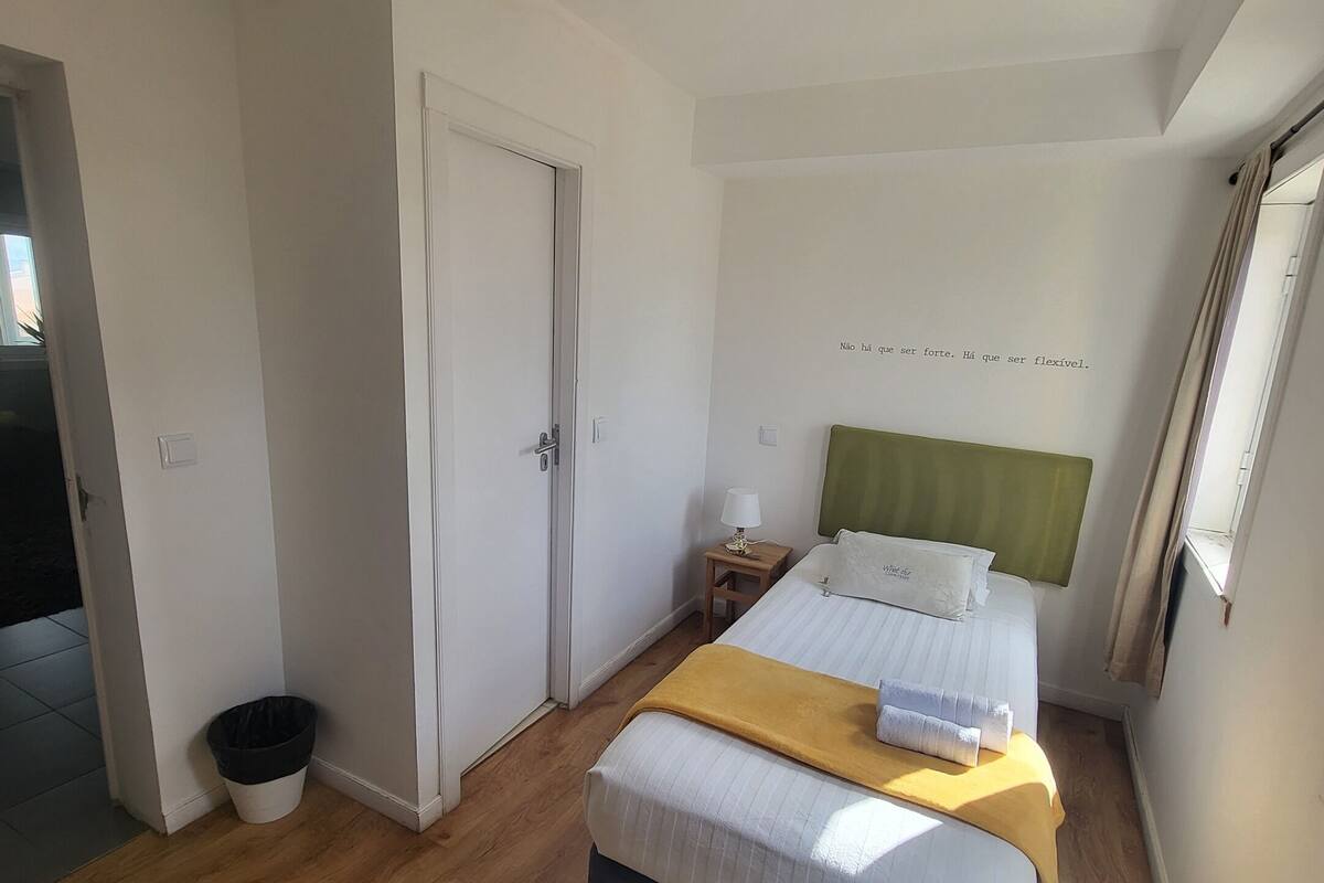 A hotel room with a bed, a nightstand, a lamp, a trash bin, and a window with curtains.