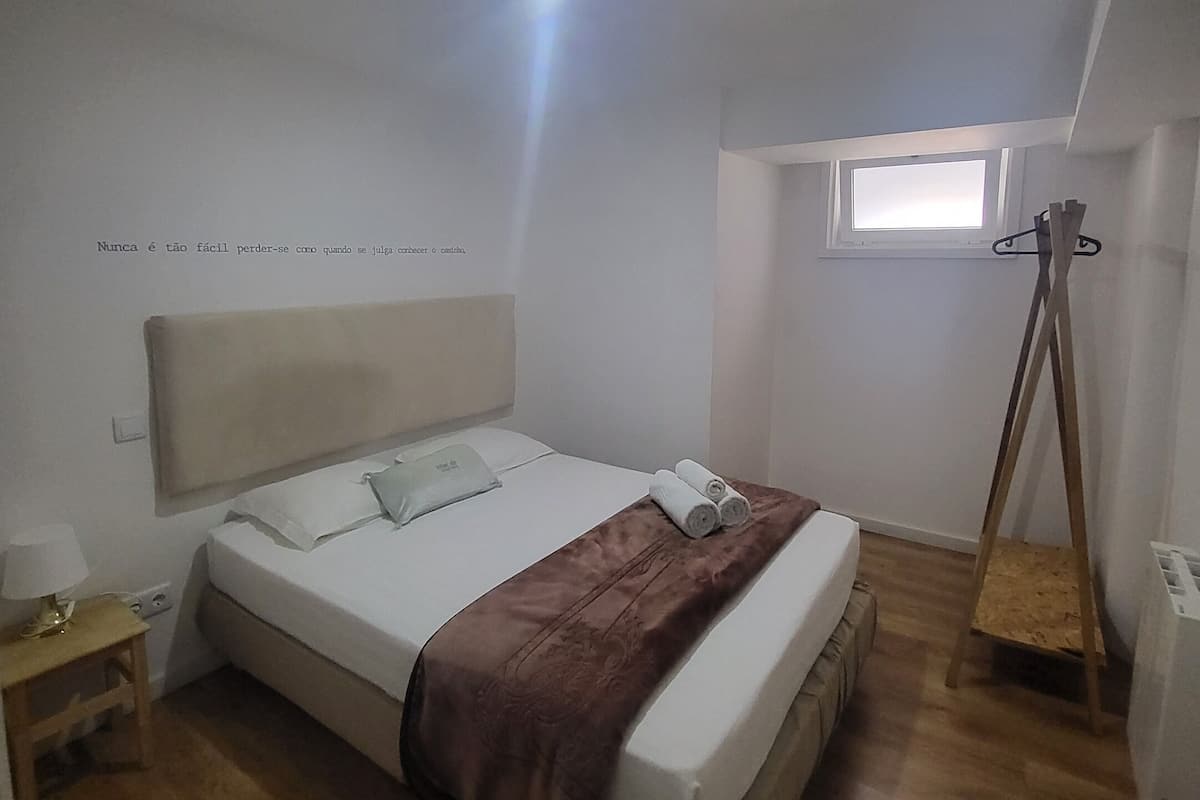 A bedroom with a bed, a bedside table, a window, and a wooden ladder.