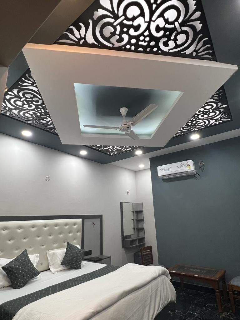Un dormitorio moderno con cabecera capitonada, cama con almohadas, ventilador de techo, iluminación empotrada, unidad de aire acondicionado y un pequeño banco de madera.