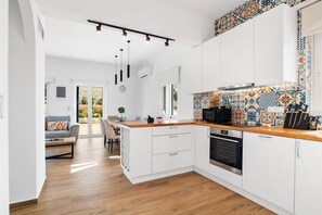 Enjoy meals in this well-equipped kitchen with oven and coffee machine, adjacent to a dining area with a table and chairs.