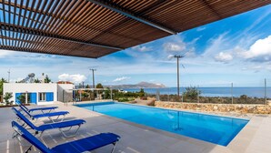 Ein Poolbereich mit blauen Liegestühlen, einer Steinmauer und Blick auf das Meer und die Berge.