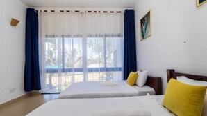 A hotel room with two beds, a large window with blue curtains, and a view of palm trees. - Lux Suites Vee Xanadu Luxury Apartments (Mombasa)