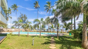 A pool area with palm trees, a stone pathway, and a building in the background. - Lux Suites Vee Xanadu Luxury Apartments (Mombasa)
