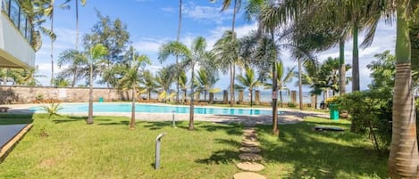 A pool area with palm trees, a stone pathway, and a building in the background.