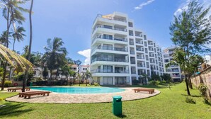 A multi-story hotel with a swimming pool, surrounded by palm trees and a grassy area with benches. - Lux Suites Vee Xanadu Luxury Apartments (Mombasa)