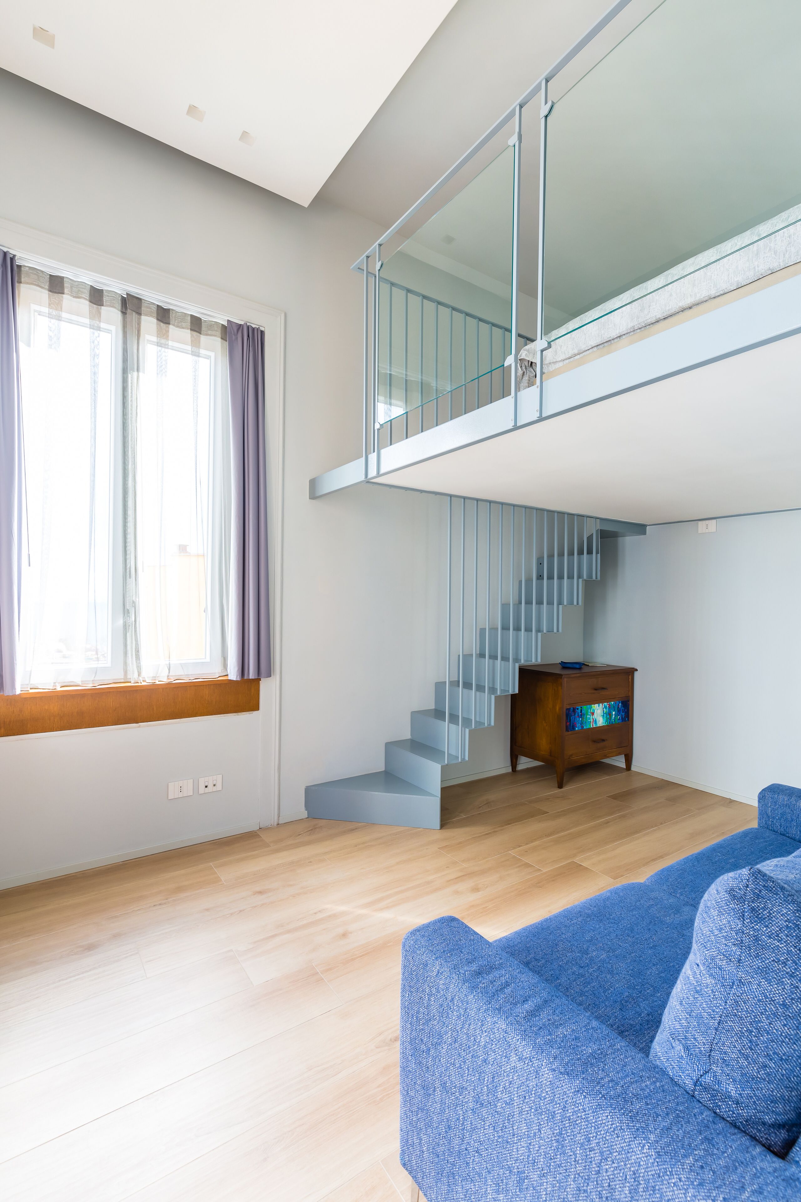 Ein modernes Wohnzimmer mit einem blauen Sofa, einem Holzschrank und einer Treppe, die zu einer oberen Etage führt.