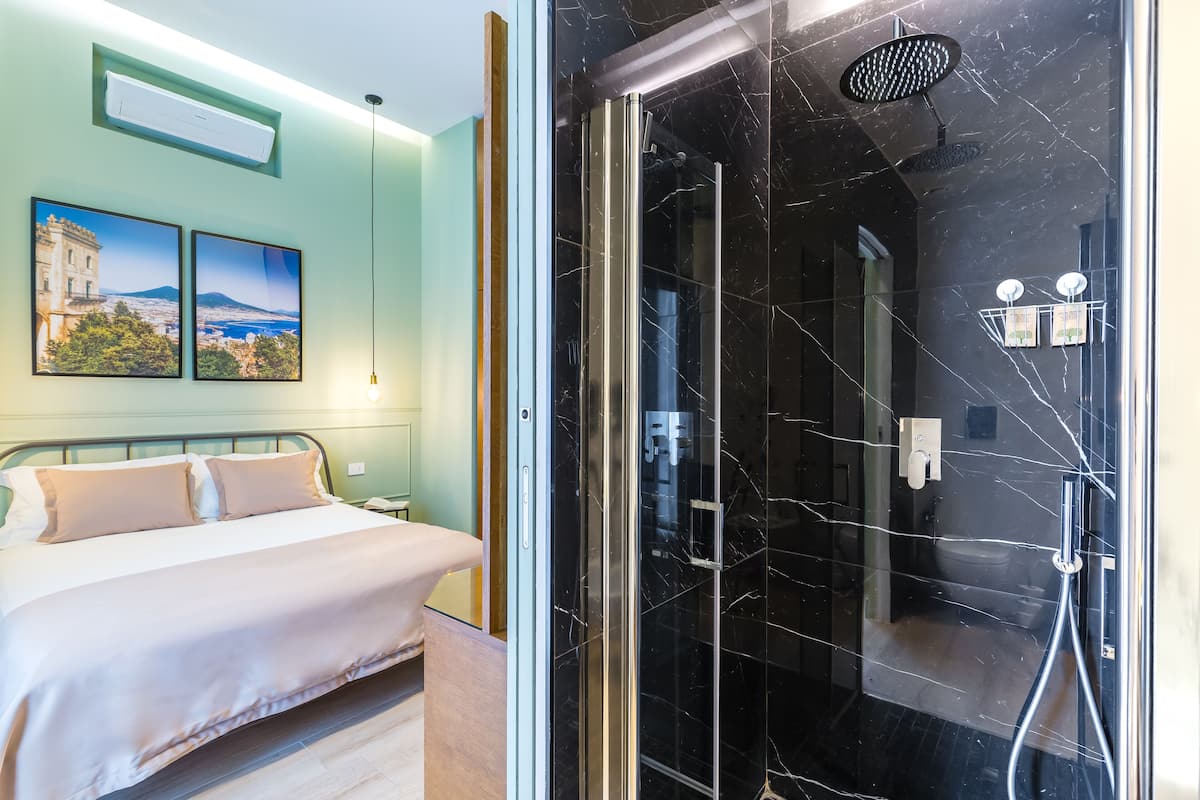 Une chambre d’hôtel avec un lit, une douche dotée d’une porte en verre et deux tableaux encadrés au mur.