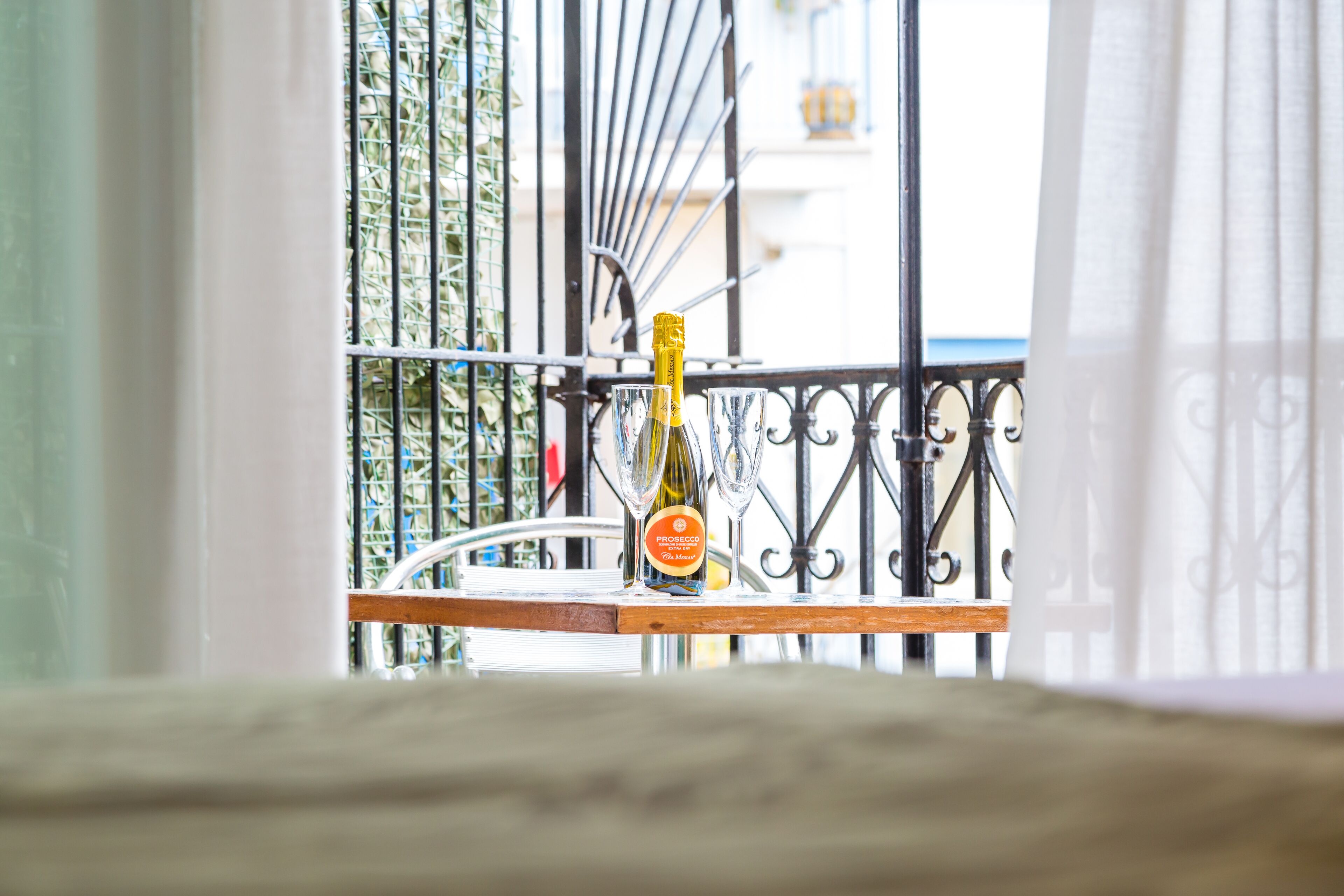 Un balcó amb una ampolla de Prosecco i dues copes sobre un banc de fusta.