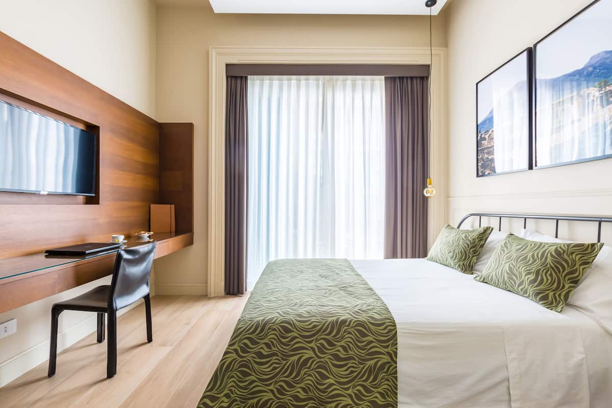 Une chambre d’hôtel avec un lit, un bureau, une chaise, une télévision et une fenêtre avec des rideaux.