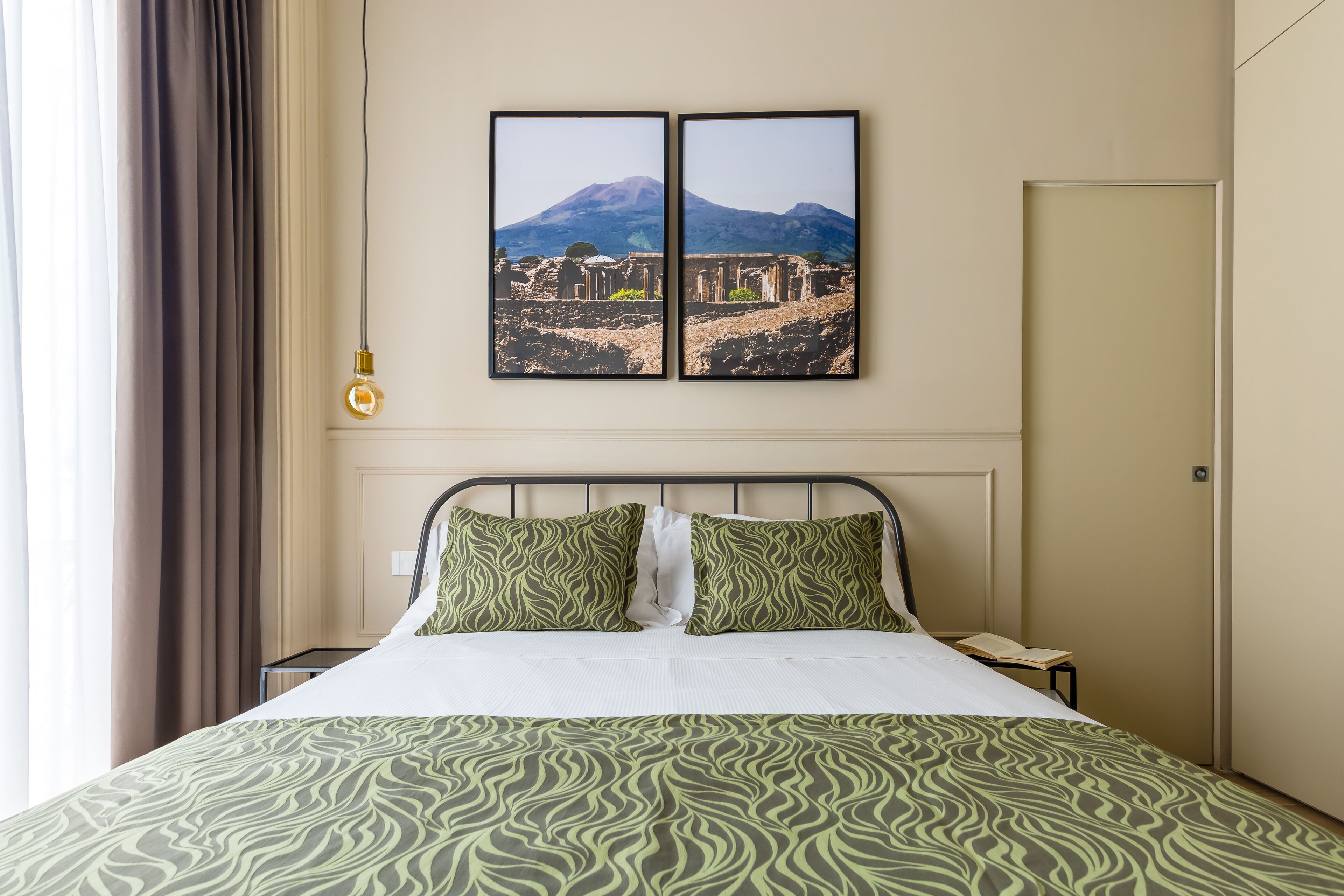 A hotel room with a bed, two wall-mounted pictures of ruins, a bedside table, and a nightstand.