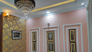 A hallway with a pink wall, a patterned wallpaper on the left, and a chandelier. - Urbanaid Uniworld (Bara Banki)