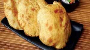 Three fried breads on a black plate with a bowl of sauce and a small bowl of sliced onions and herbs. - Urbanaid Uniworld (Bara Banki)
