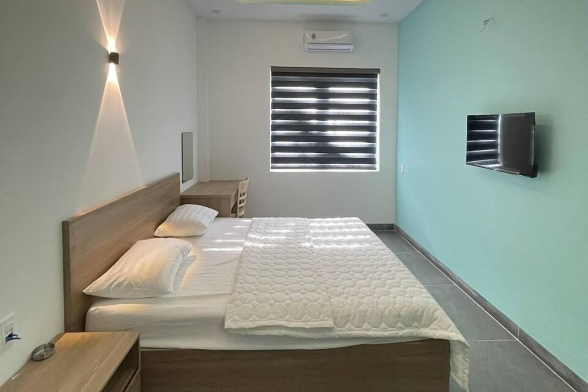 Un dormitorio moderno con cama, mesitas de noche, una ventana con persianas, equipo de aire acondicionado y televisor de pared.