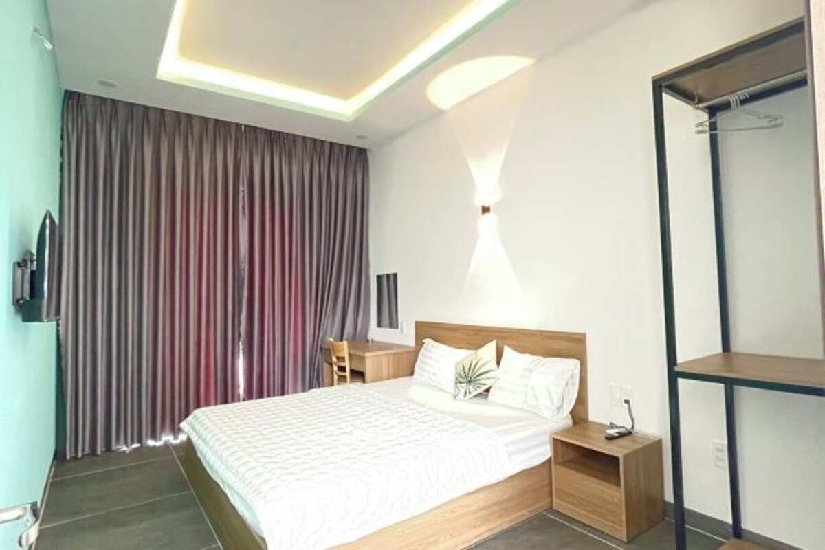 A modern hotel room with a large bed, a desk, and a wardrobe.