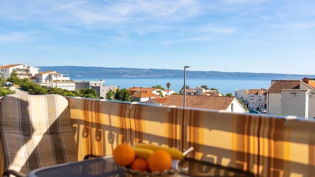 A balcony with a view of the sea, a chair, and a bowl of fruit. - Coastal Comfort Apartment (Podstrana)