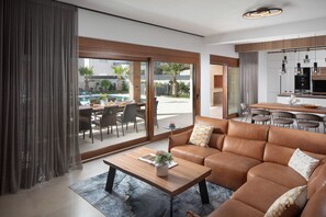 Relax in a spacious living area with a comfortable sofa and coffee table, offering a view of the pool and lush greenery through large sliding doors.