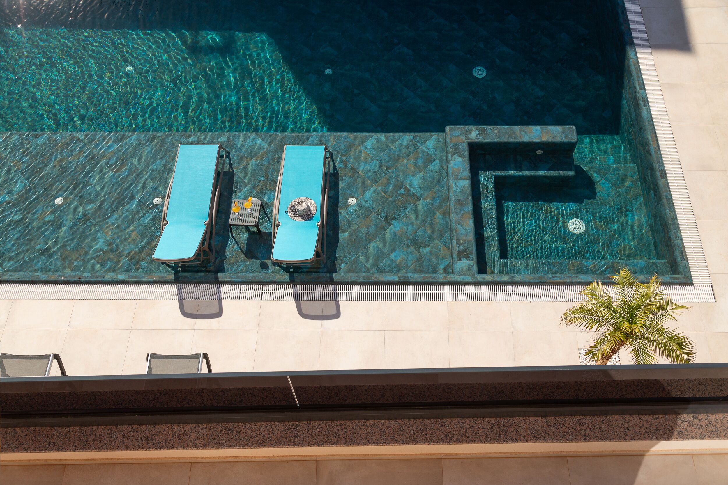 Vue aérienne d’une piscine avec deux chaises longues et un palmier.