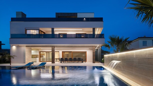 Et moderne hus med to etager, en swimmingpool, udendørs møbler og et vandfald.