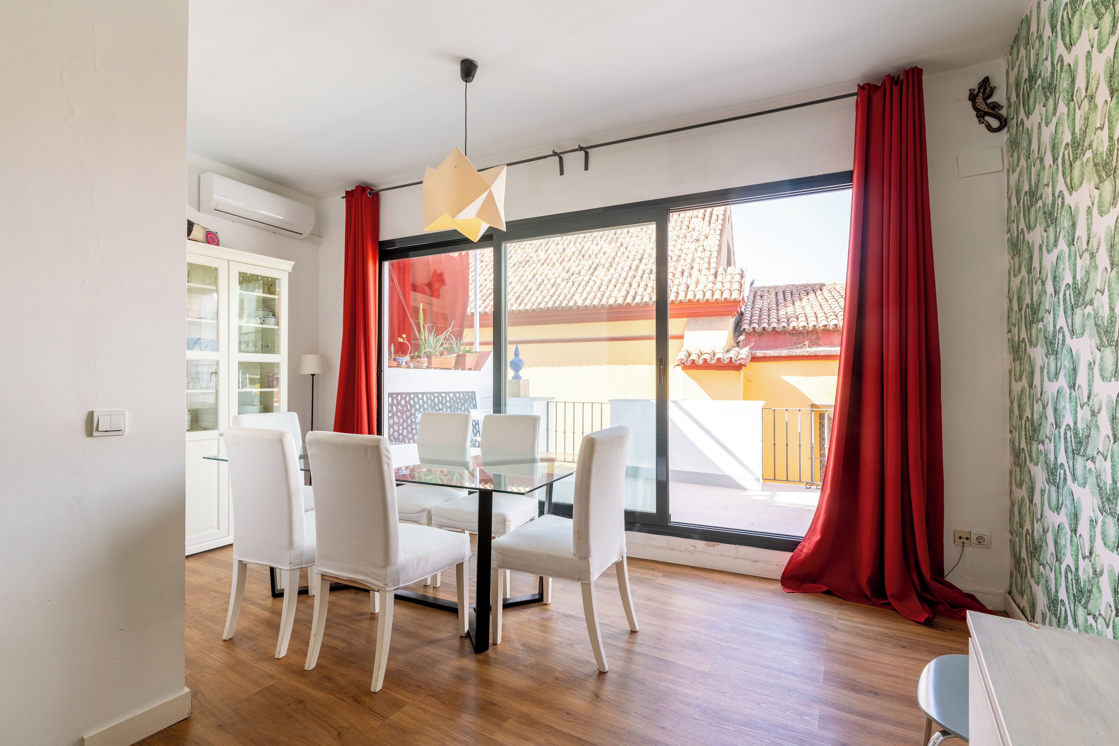 Un comedor con mesa de vidrio y sillas blancas, un armario blanco y una cortina roja.