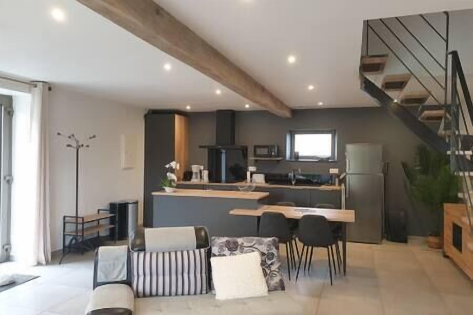 A modern kitchen with a central island, a dining area with a sofa and chairs, and a staircase leading to an upper level.