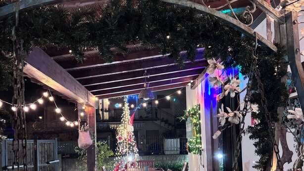 Un espace extérieur aménagé en terrasse, avec une pergola en bois, des guirlandes lumineuses et un sapin de Noël.