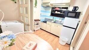 A compact kitchen with a microwave, sink, and a refrigerator. There is a small table with a vase of flowers and a book. - Grand Colbert NANBA 505, 605, 704 (Osaka)