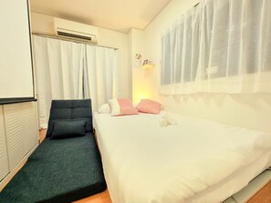 A bedroom with a bed, a chair, an air conditioning unit, and a window with sheer curtains. - Grand Colbert NANBA 505, 605, 704 (Osaka)