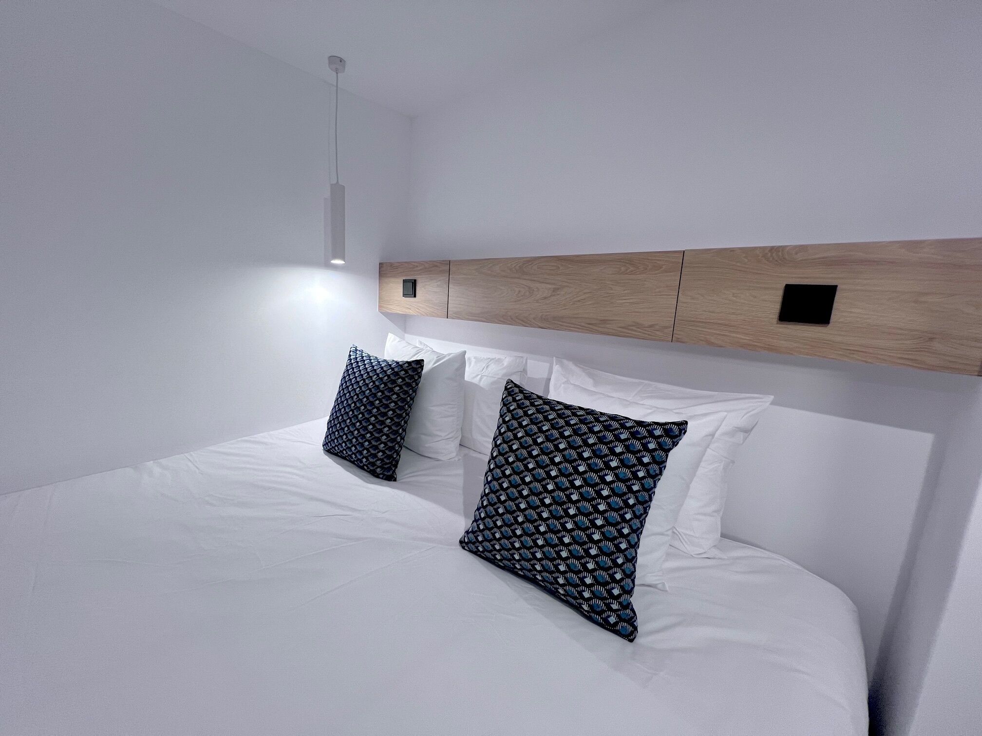 Una habitación de hotel moderna con una cama grande, ropa de cama blanca y dos almohadas estampadas.