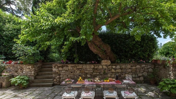 An outdoor patio with a stone wall, a table set with food, and chairs. - Apartment in historic villa with swimming pool near Florence (Sesto Fiorentino)