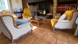 Un salon chaleureux avec une cheminée, deux fauteuils, un canapé et une table basse.