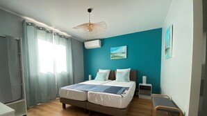 Une chambre à coucher comprenant un lit, une table de chevet, une chaise, un luminaire suspendu et un tableau accroché au mur.