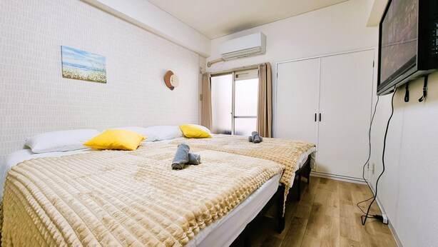 Une chambre d’hôtel avec deux lits, une télévision, un climatiseur et une fenêtre avec des rideaux.