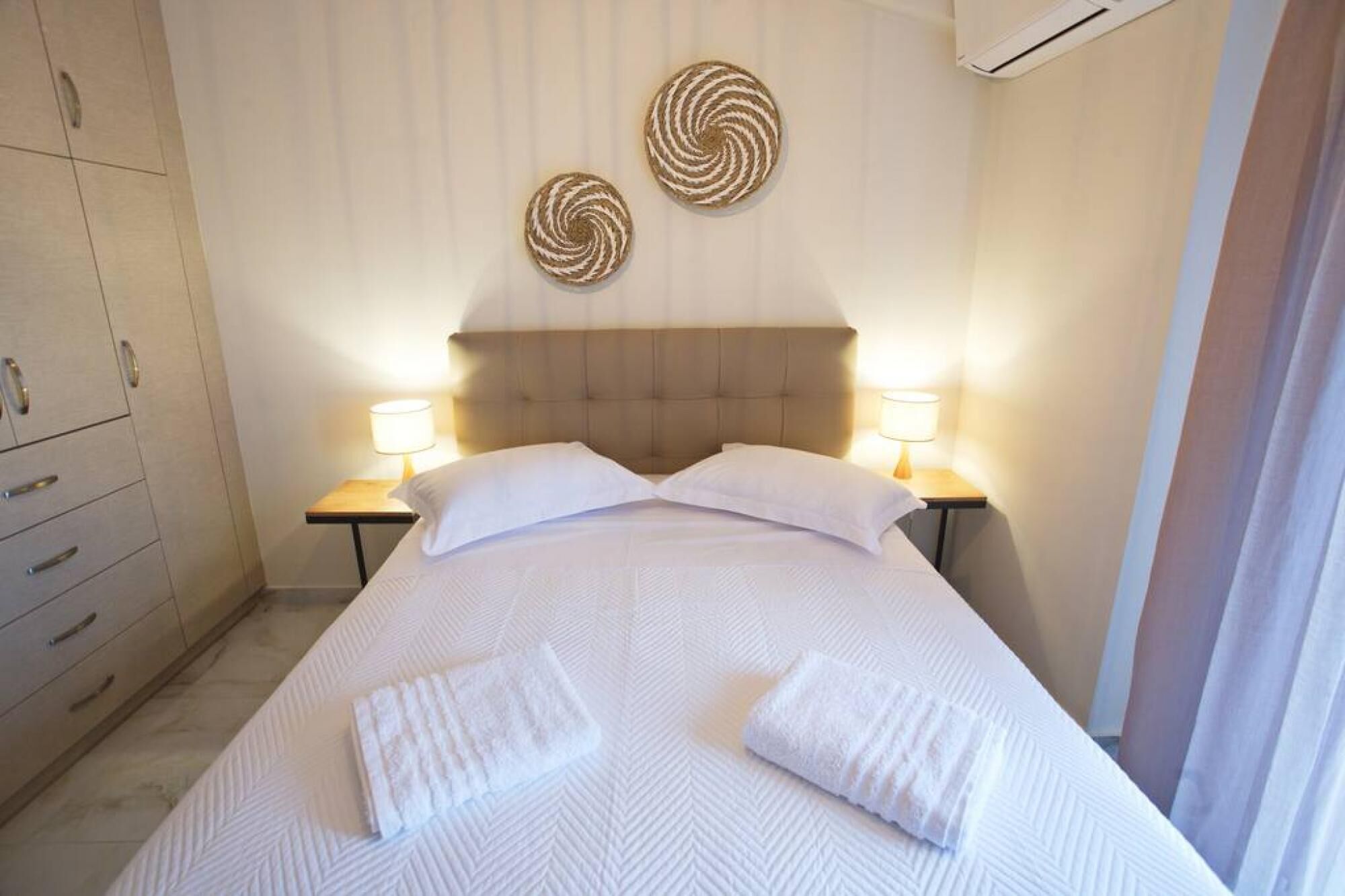 Habitación de hotel con una cama grande, dos lámparas de noche, un cabecero y dos elementos decorativos en la pared.