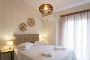Quarto de hotel com uma cama, duas luminárias na parede, uma luz de teto, ar condicionado e uma janela com cortinas.