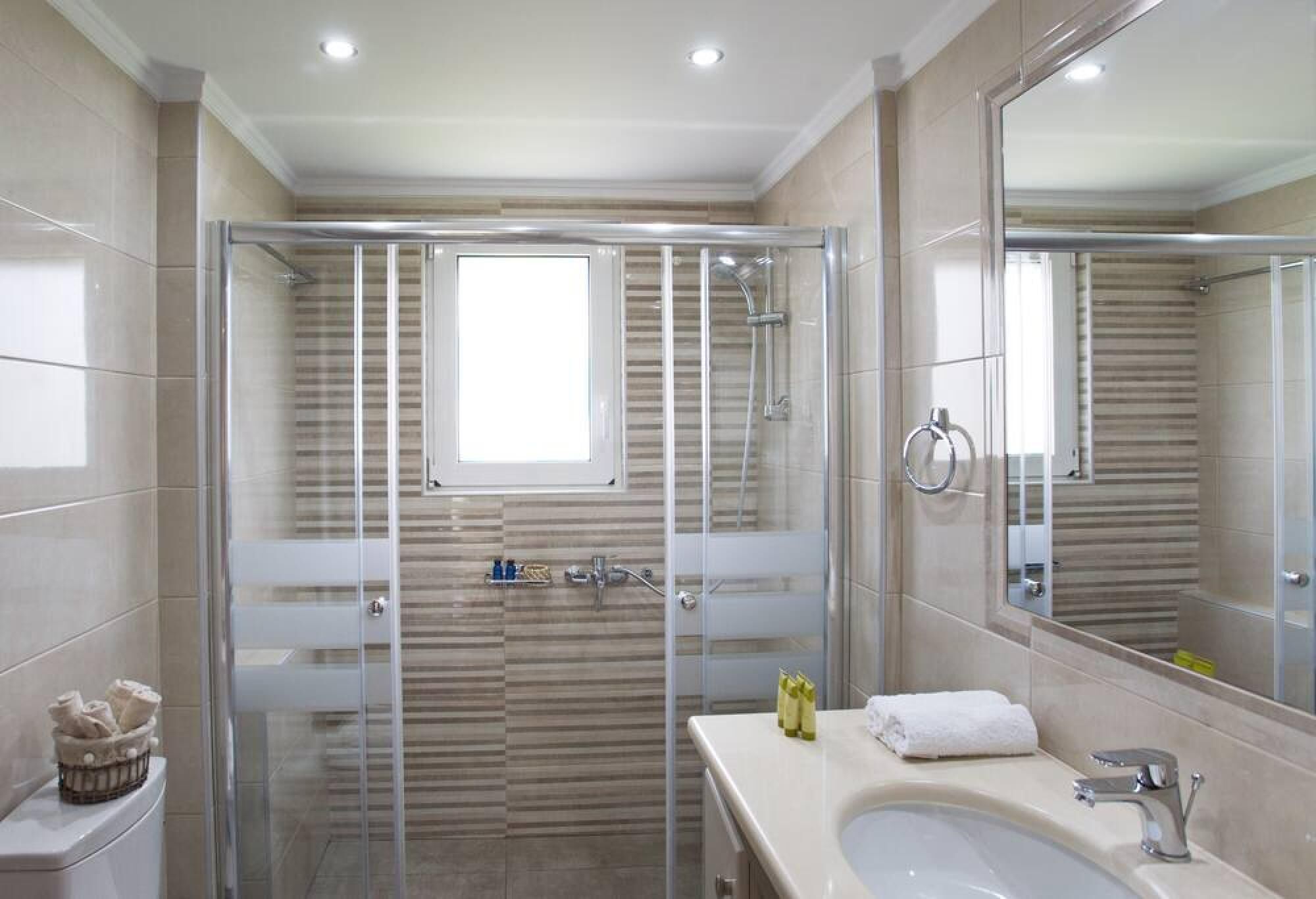 A modern bathroom with a glass-enclosed shower, a large mirror, and a sink with a towel.