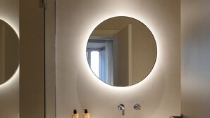 Un baño moderno con un espejo redondo, un lavamanos y una cabina de ducha con mampara de cristal.