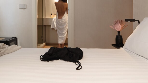 Un dormitorio con cama, mesita de noche, lámpara y baño visible a través de una puerta abierta.