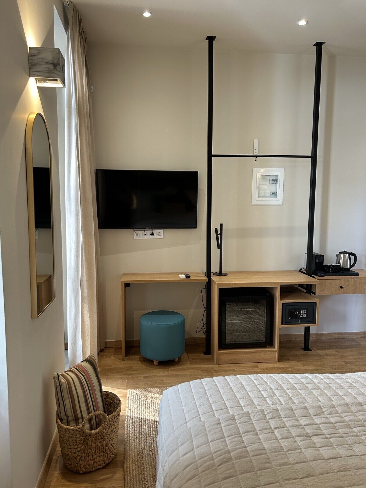 A modern hotel room with a large bed, a desk with a computer, a television, and a small kitchenette.