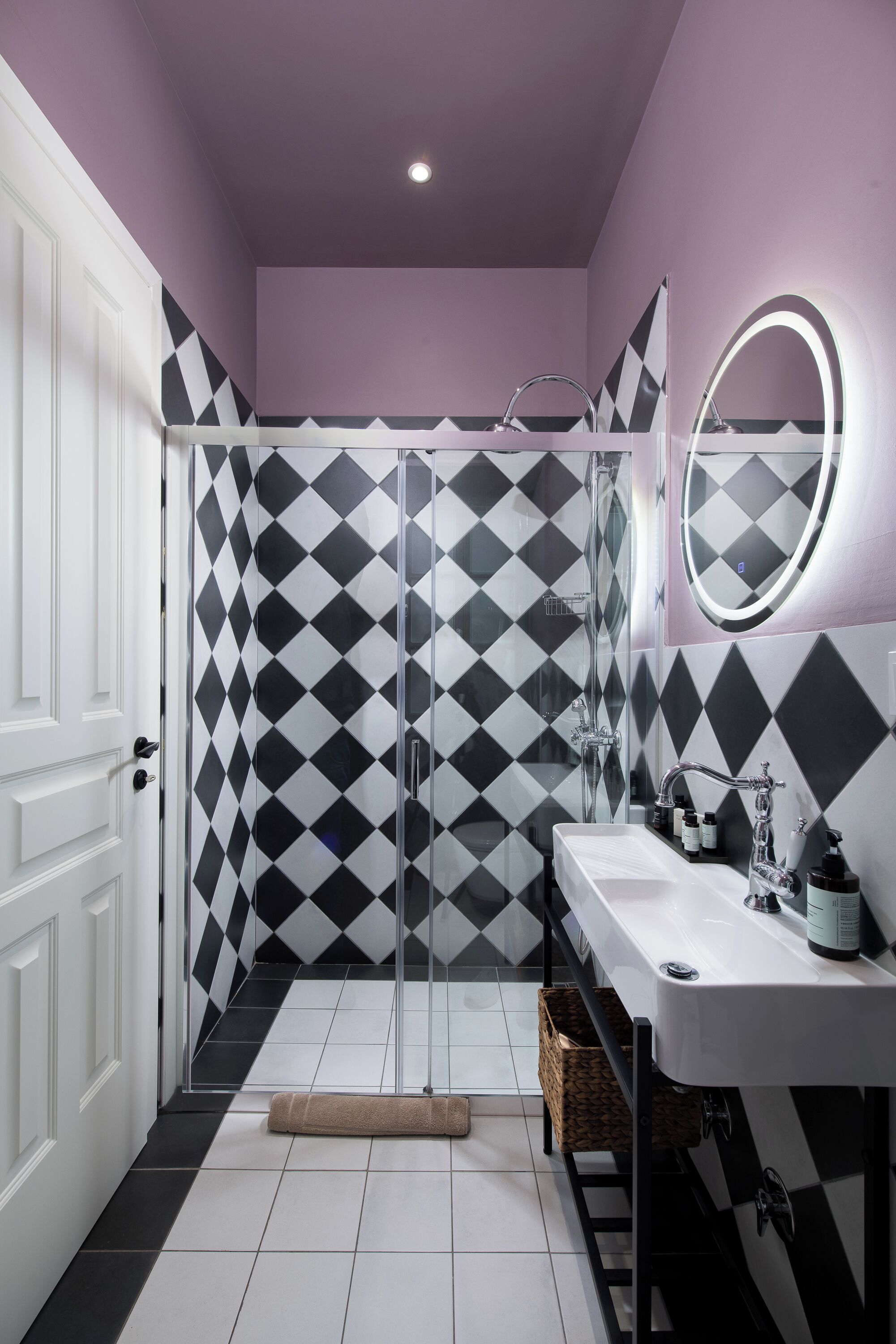 A bathroom with a black and white diamond-patterned shower wall, a white sink with a mirror, and a white door.