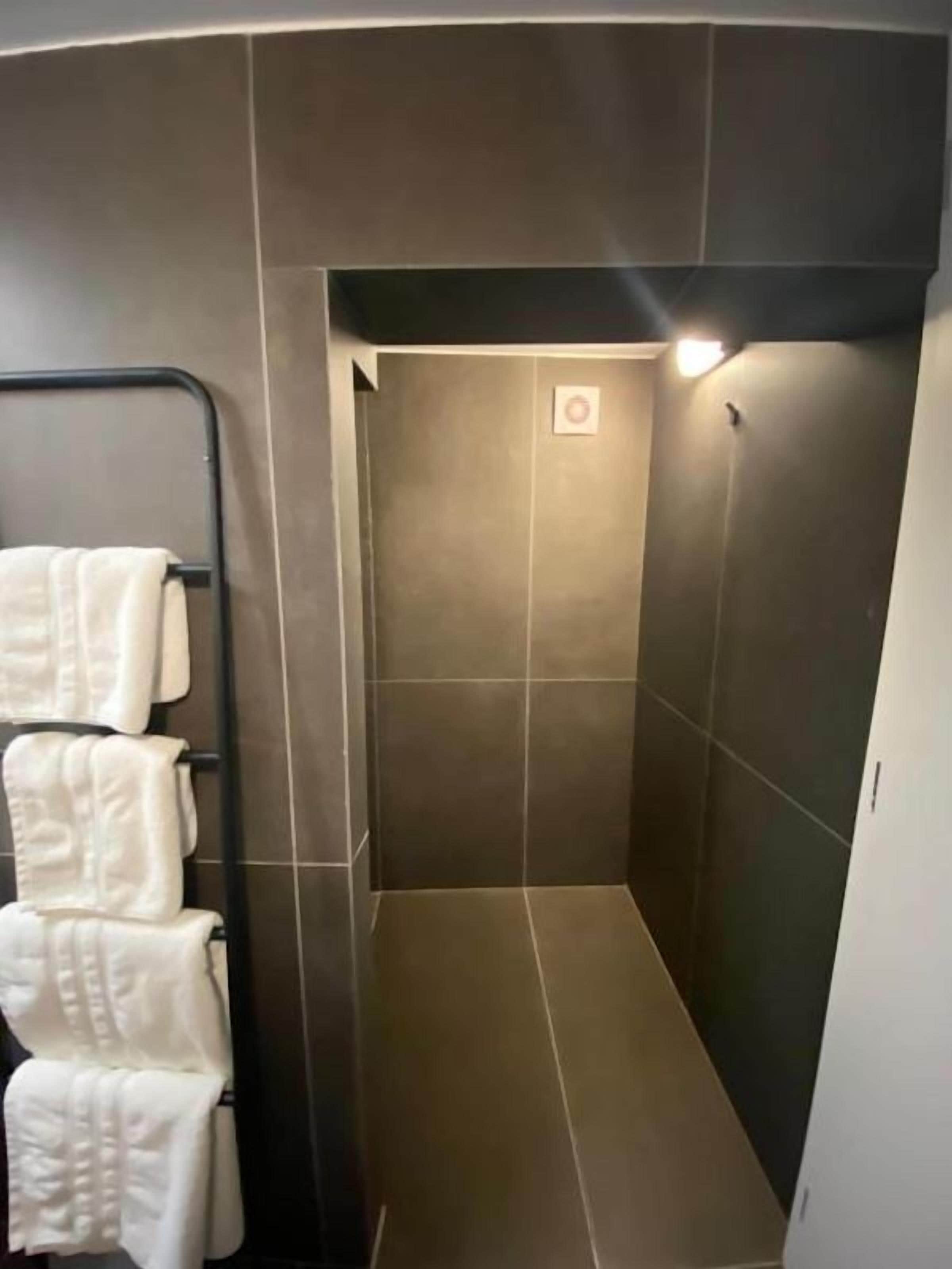 Un espacio de ducha estrecho, con azulejos y un perchero a la izquierda.