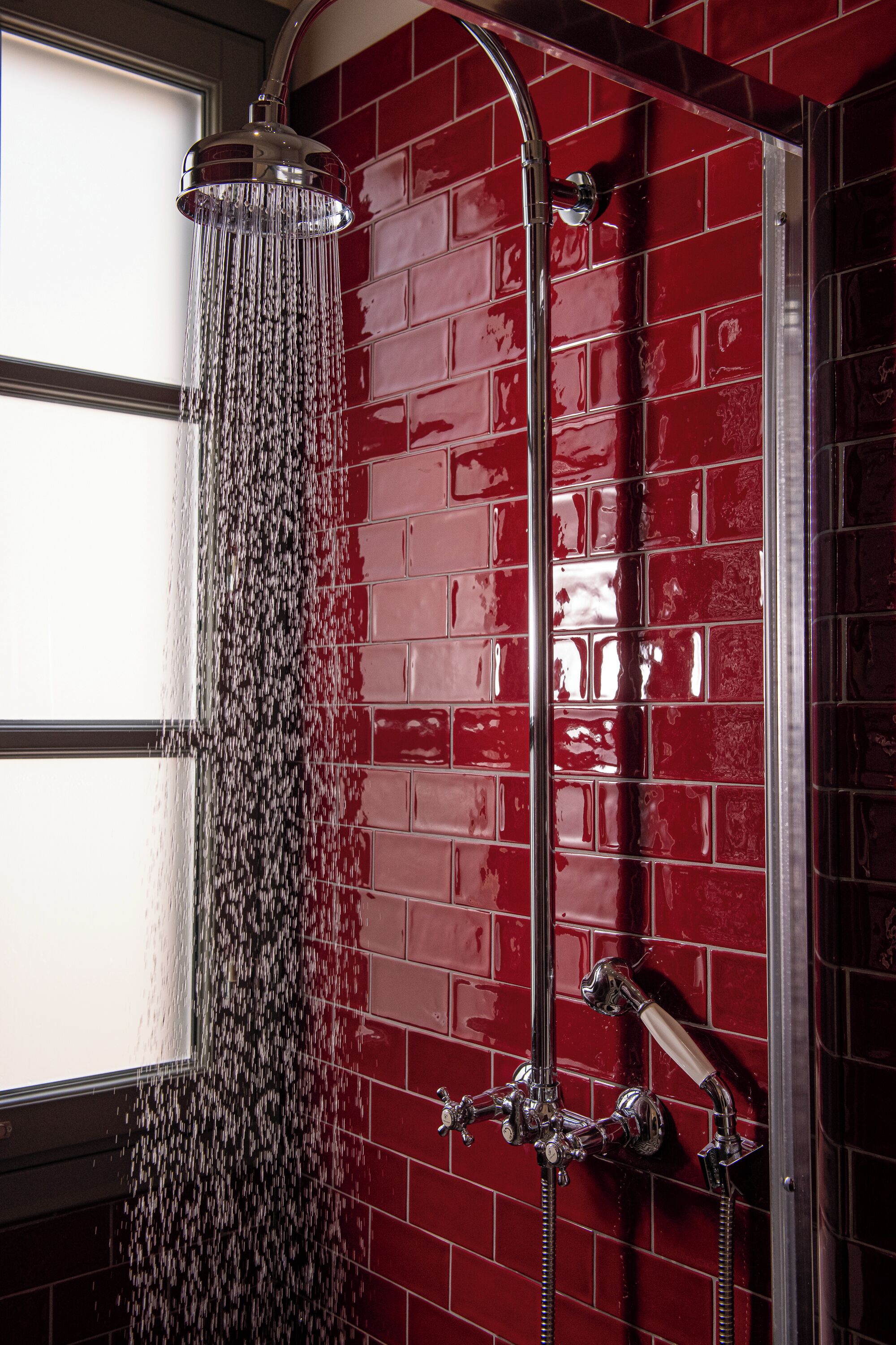 Eine Dusche mit Duschkopf aus Chrom und mehreren Düsen vor einer roten Fliesenwand.